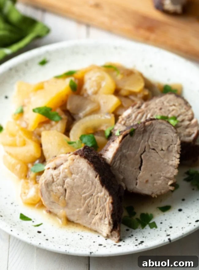 Slices of succulent pork tenderloin, glistening with a savory glaze, served alongside tender apples and caramelized onions on a white speckled plate.