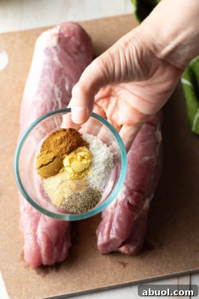 Two raw pork tenderloins resting on a cutting board, with a hand gently sprinkling a bowl of mixed spices over them, preparing for the seasoning rub.