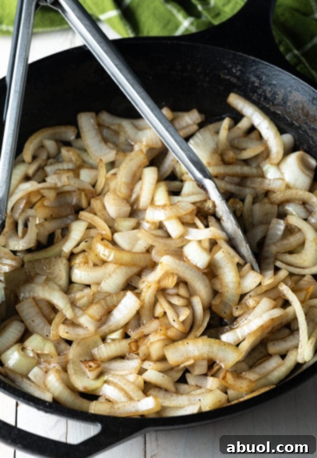 Sliced onions gently sautéing in a hot skillet with tongs, developing a beautiful translucent texture.