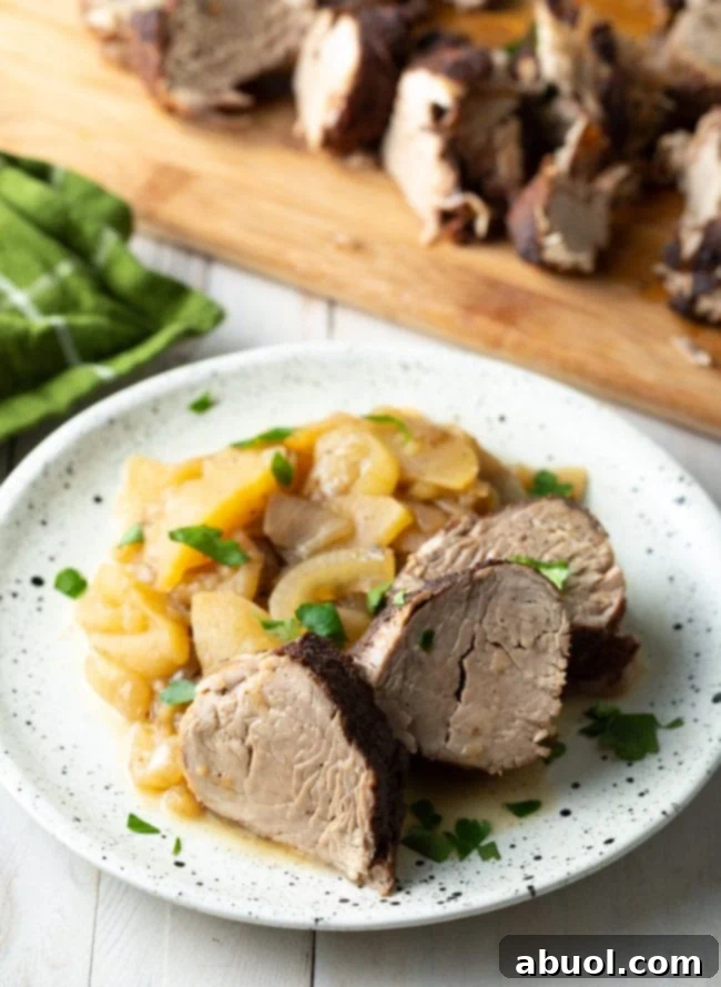 Succulent slices of pork tenderloin artfully arranged with tender, caramelized apples and onions, served on a pristine white plate, showcasing a delightful blend of colors and textures.