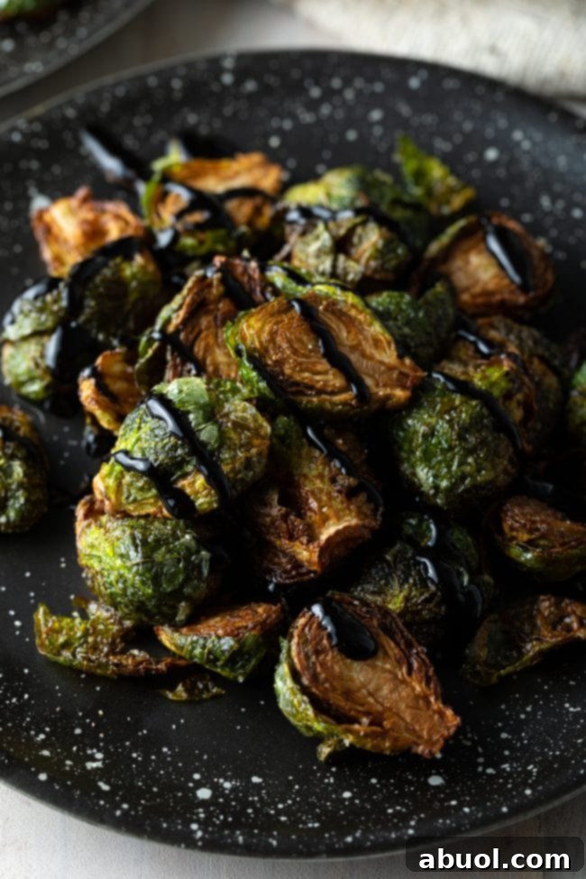 Fried Brussels sprouts with balsamic glaze beautifully arranged on a black speckled plate.