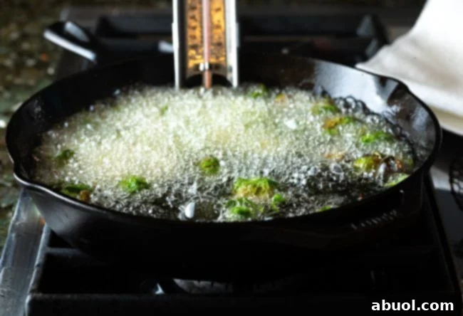 Brussels sprouts actively frying in hot oil within a large skillet.