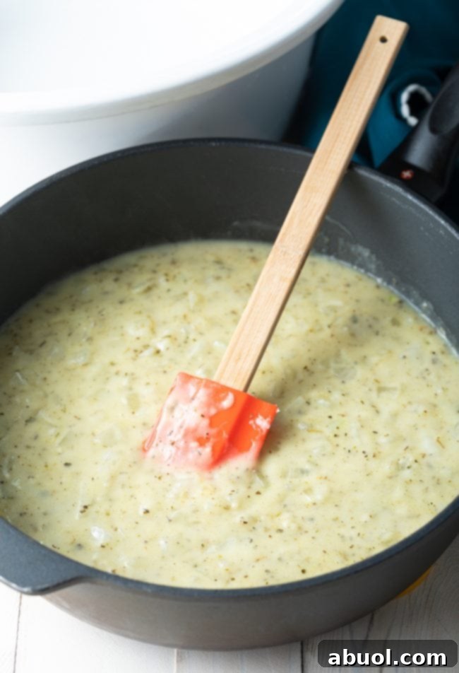 A golden roux cooking in a skillet, being stirred with a rubber spatula.