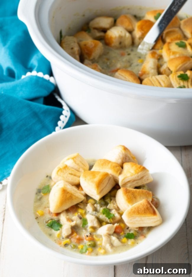 A serving of Crock Pot Chicken Pot Pie in a white bowl, generously topped with pieces of fluffy biscuits.