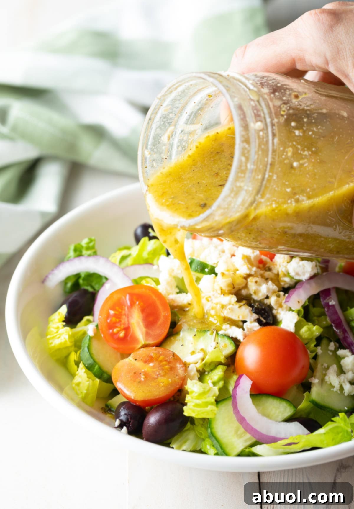Zesty Homemade Greek Dressing 2 A hand pouring a glass of Greek Salad Dressing over a Greek Salad, showcasing its rich texture and color.