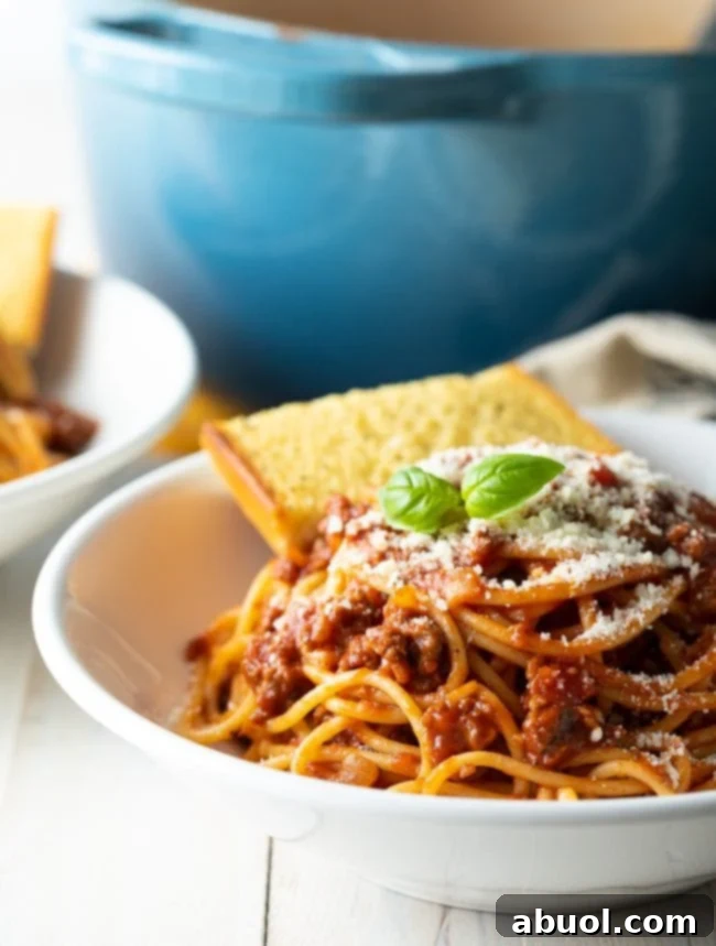 Spaghetti with homemade meat sauce served in a white bowl, accompanied by garlic bread