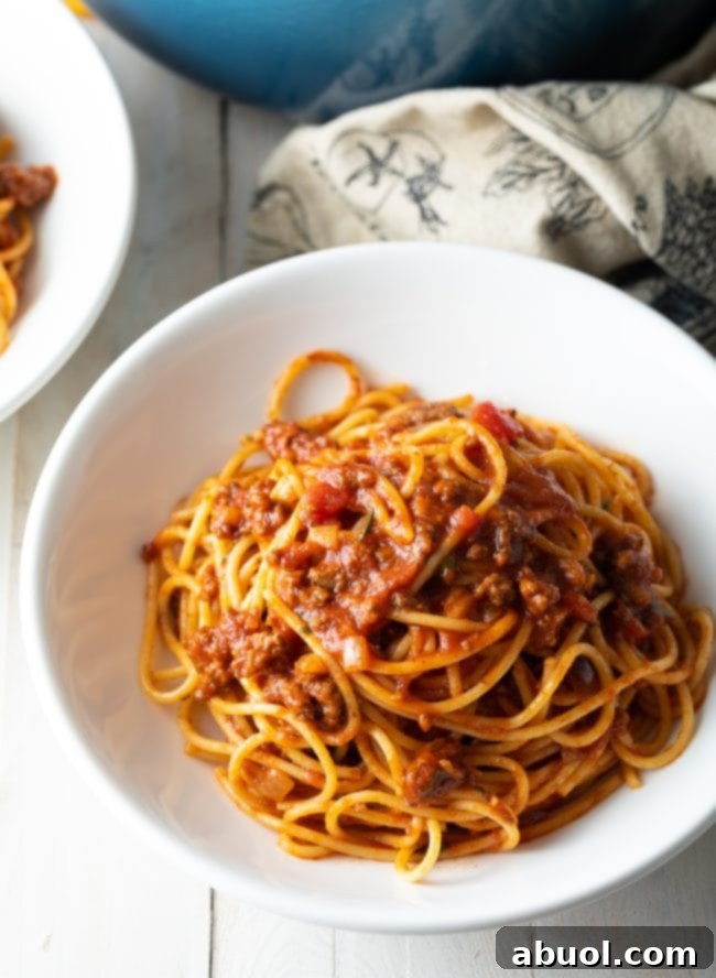 A serving of spaghetti and meat sauce in a white bowl, garnished with fresh herbs