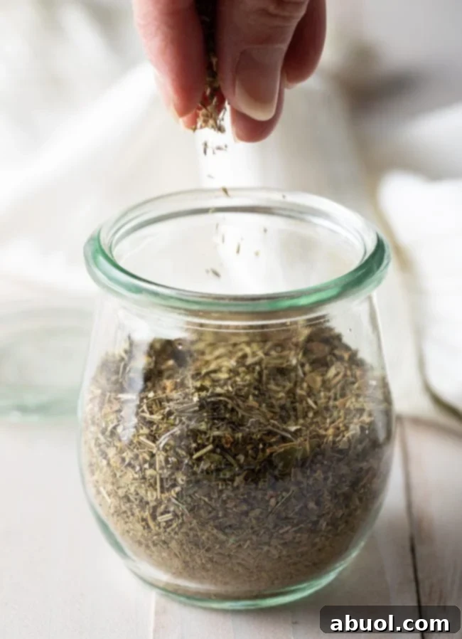 Homemade Italian seasoning in a jar with dried herbs scattered around