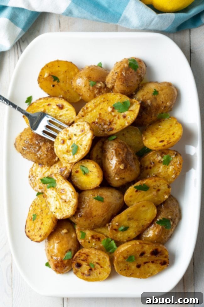 Greek lemon garlic potatoes overhead on a white plate. A fork is holding one of the potatoes, showing its crispy exterior and tender interior.