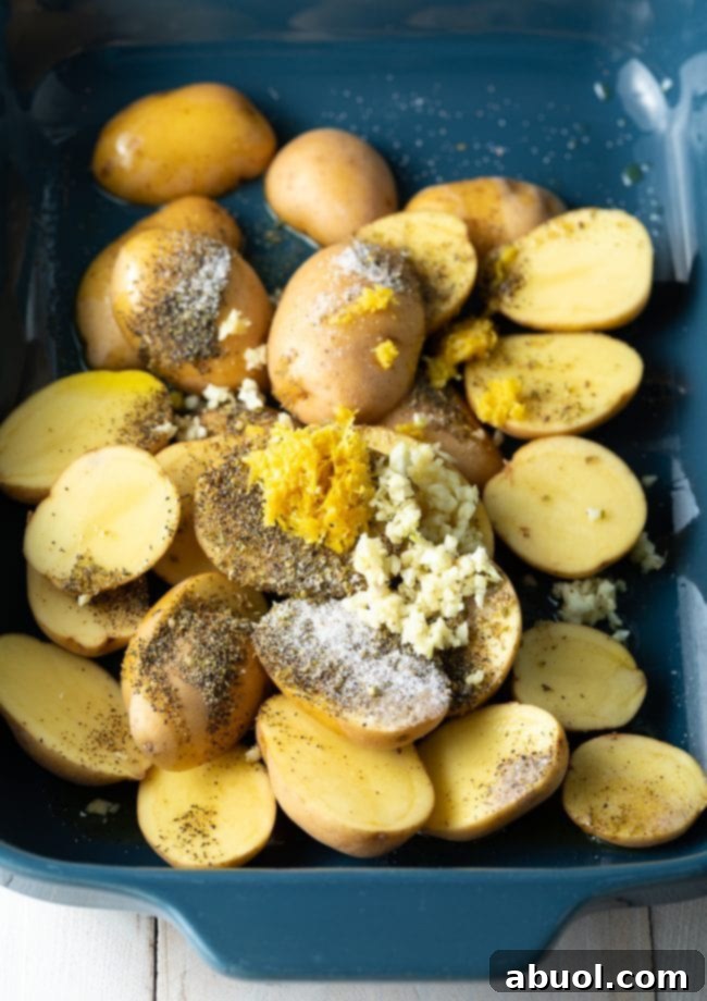 Potatoes, garlic, lemon, and oregano ready for roasting in a blue baking dish.