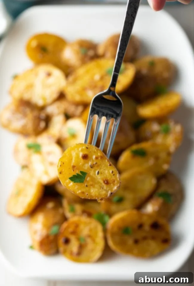 Close up of a fork holding up a garlic potato with parsley sprinkled on it, emphasizing the texture and seasoning.