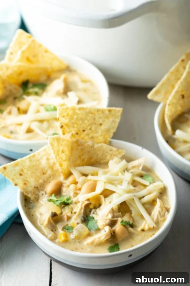 creamy white chicken chili recipe in blue and white bowls with tortilla chips and cheese on top