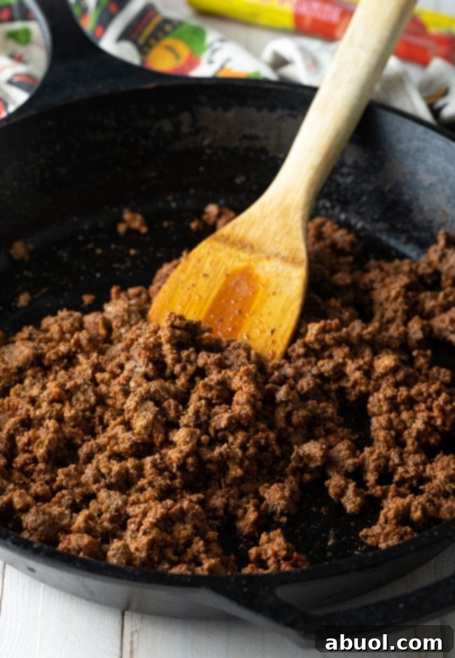 Ground beef browning in a large skillet with a wooden spatula.