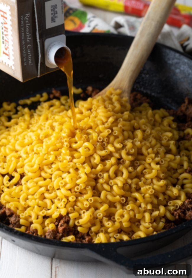 Uncooked macaroni noodles and beef broth added to the skillet with browned ground beef.