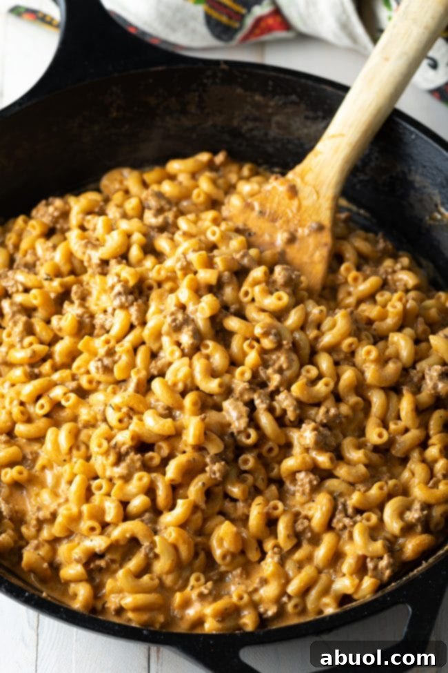 A wooden spatula stirs the finished cheeseburger hamburger helper macaroni in a single pot.