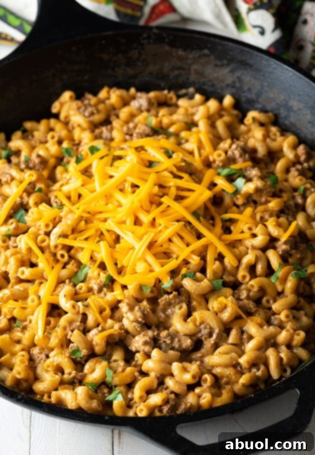 Homemade mac and cheese hamburger helper in a skillet, garnished with fresh parsley and shredded cheddar.