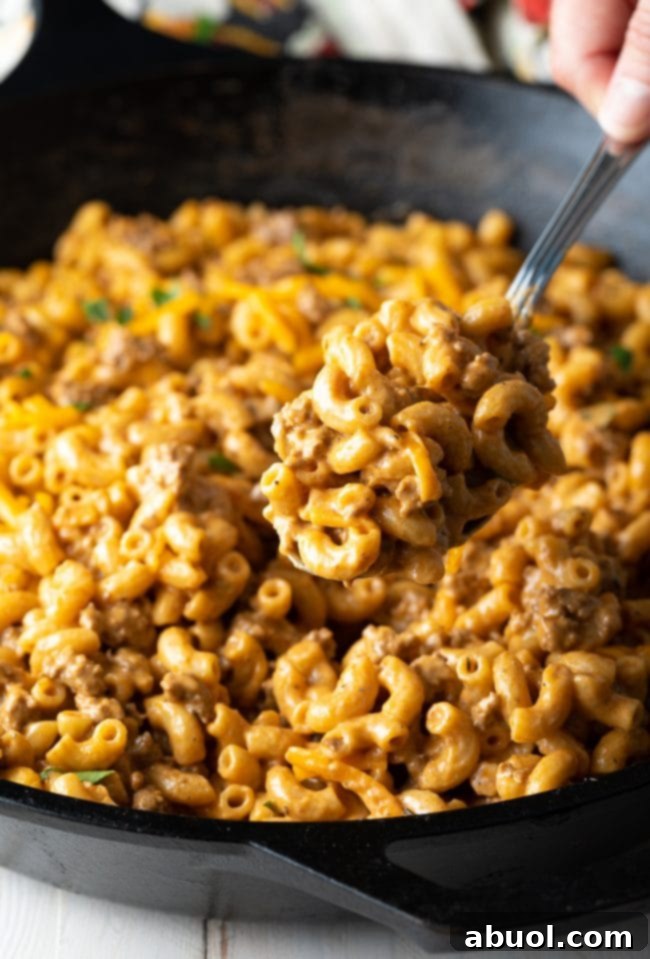A spoonful of homemade cheeseburger mac and cheese being lifted from the skillet.