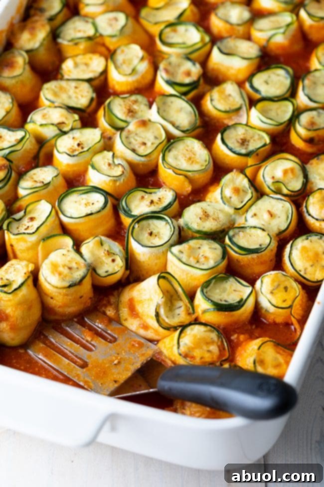 keto zucchini lasagna roll ups in a baking dish with a spatula in the dish. 