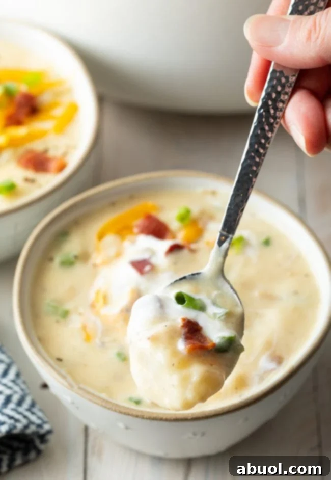 Cozy Stovetop Potato Soup 5 A close-up of a bowl of chunky potato soup, with a hand holding a spoon ready to scoop a delicious bite.