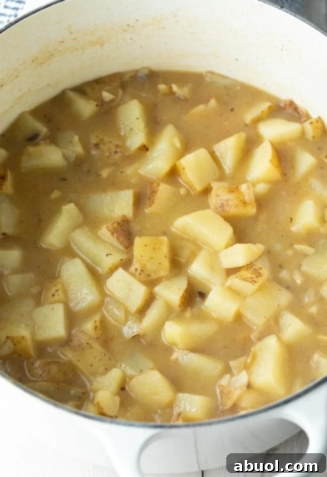 Cozy Stovetop Potato Soup 6 Chopped russet potatoes simmering in rich chicken broth within a large Dutch oven.