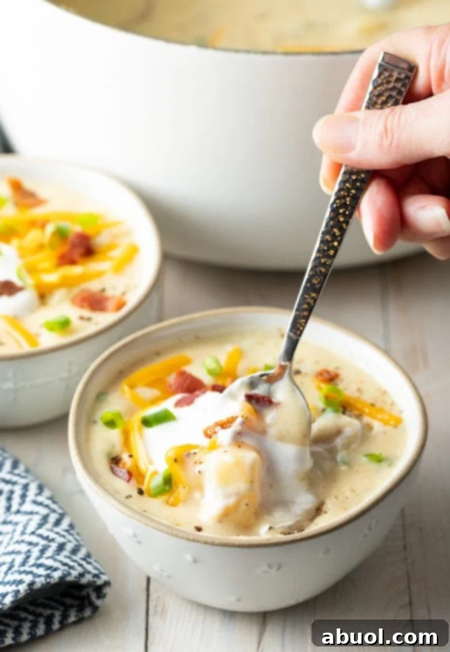 Cozy Stovetop Potato Soup 10 A hand holding a spoon, poised to enjoy a spoonful of creamy potato soup from a rustic bowl.