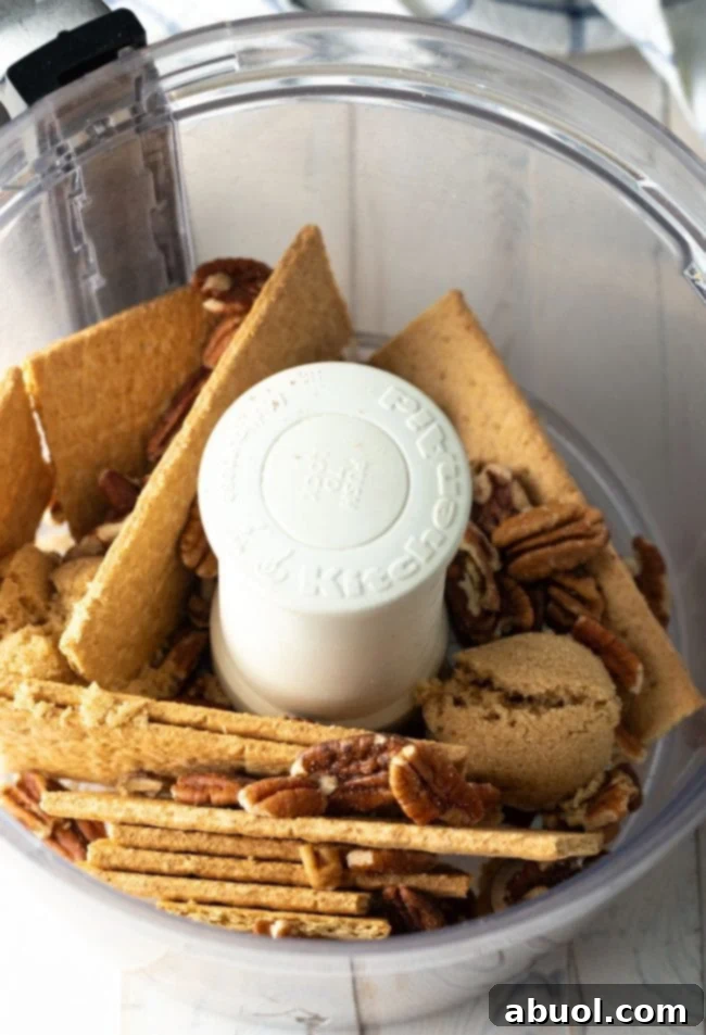 Graham crackers and pecans being processed together in a food processor, creating the base for the crust.
