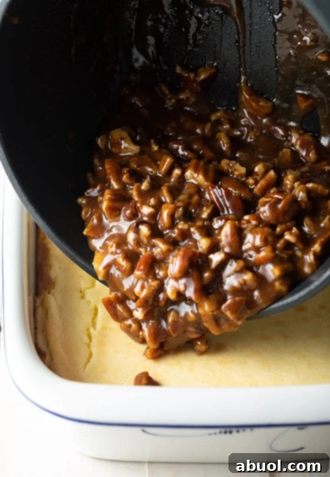 The warm caramel pecan topping being artfully poured over the cooled cheesecake in a baking dish.