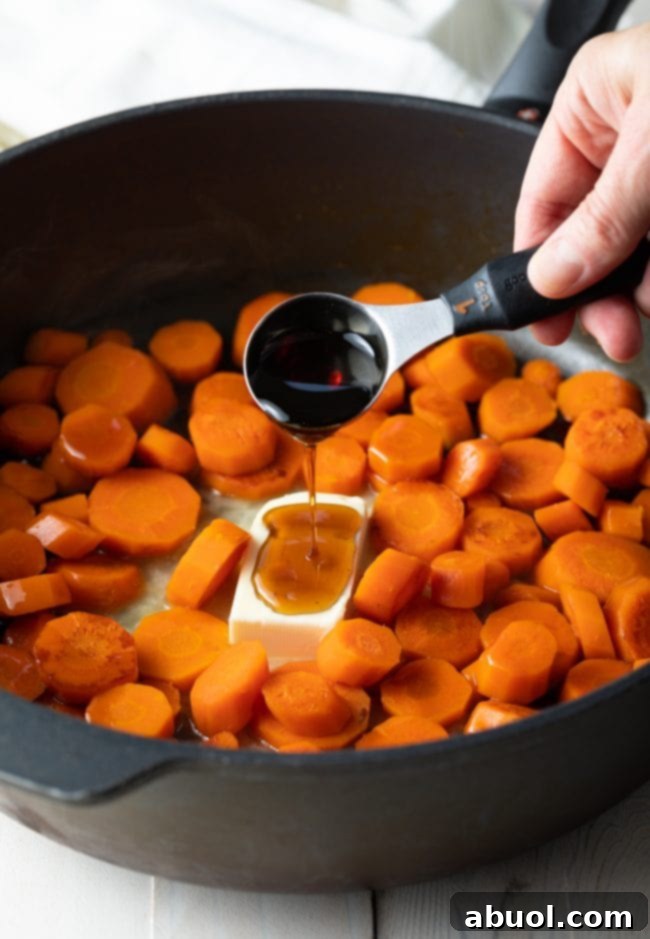 Adding butter and maple syrup to steamed carrots in a pan to create the rich glaze.