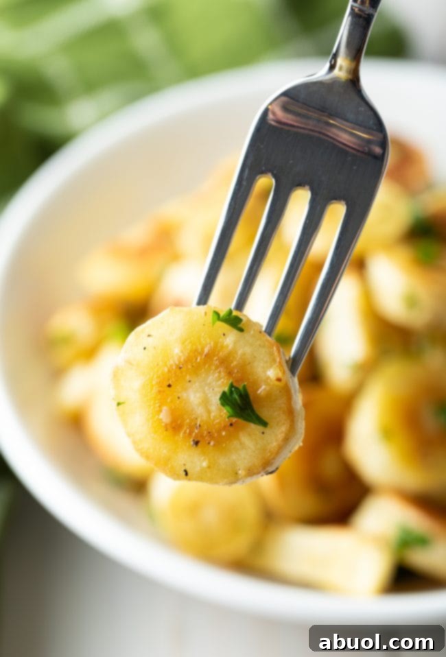 Savory Garlic Butter Parsnips 4 A single piece of perfectly roasted parsnip, garnished with fresh parsley, held by a fork.