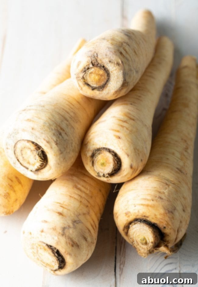 Savory Garlic Butter Parsnips 5 Close-up view of fresh, raw parsnips, garlic cloves, and a sprig of parsley, prepared for cooking.