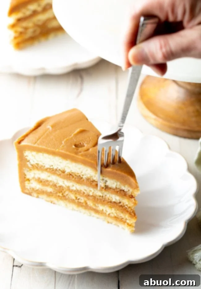 four layers of white cake with a thick salted caramel frosting and a fork ready to cut off a bite