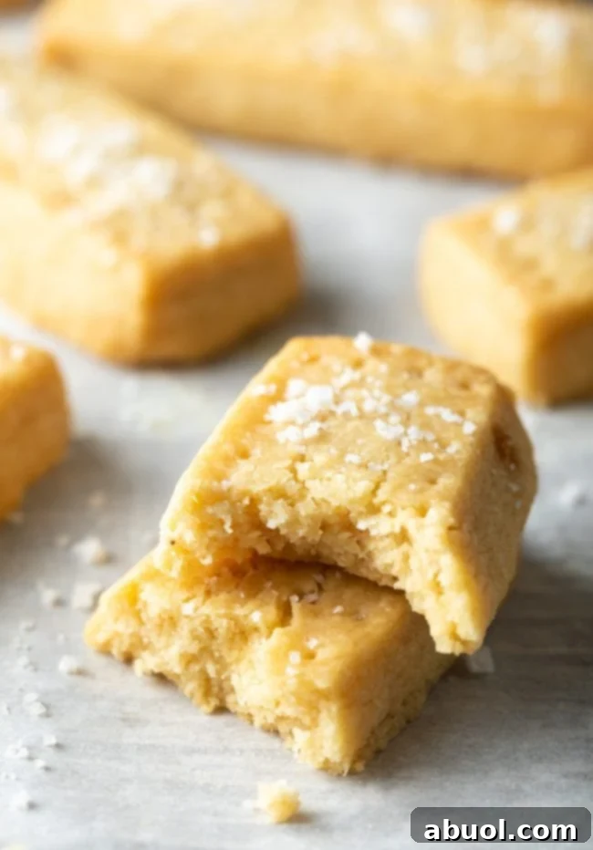 A stack of golden Scottish shortbread cookies, with one cookie showing a bite taken out, highlighting its tender crumb.