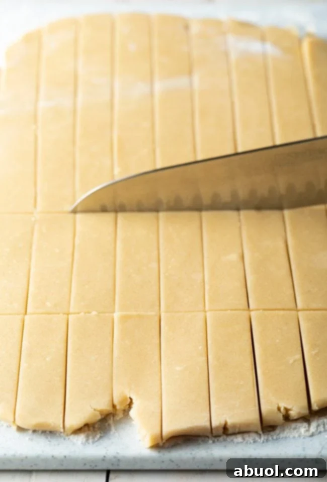 A large chef's knife precisely slicing the shortbread dough into uniform small rectangles.