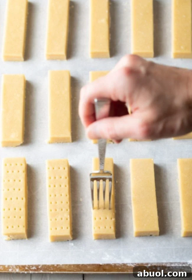 A hand gently poking holes with a fork into unbaked shortbread dough, ready for the oven.