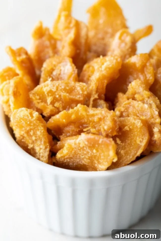 A small, inviting bowl filled with glistening homemade ginger candies, known for easing nausea and providing a sweet-spicy delight.