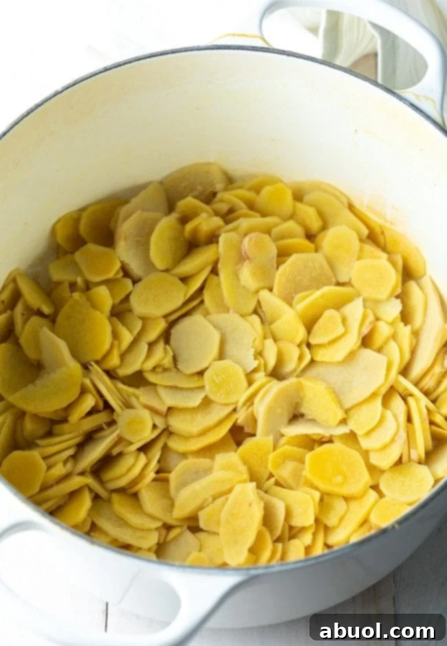Peeled and uniformly sliced ginger pieces resting in a large Dutch oven, ready to be simmered in water.