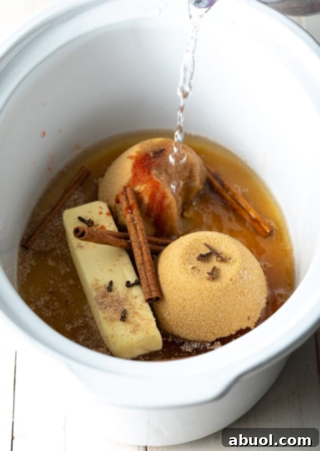 Close-up of a rustic wooden surface with dried cinnamon sticks, whole cloves, and a small pile of ground nutmeg, evoking the aromatic spices used in hot buttered rum.