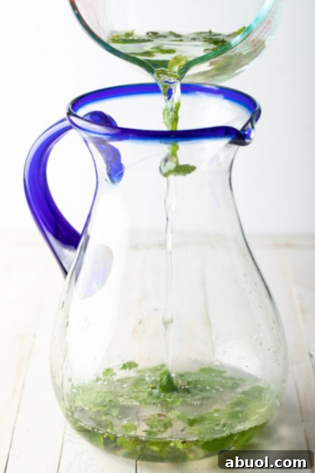Simple syrup being poured into a large pitcher with other mojito ingredients.