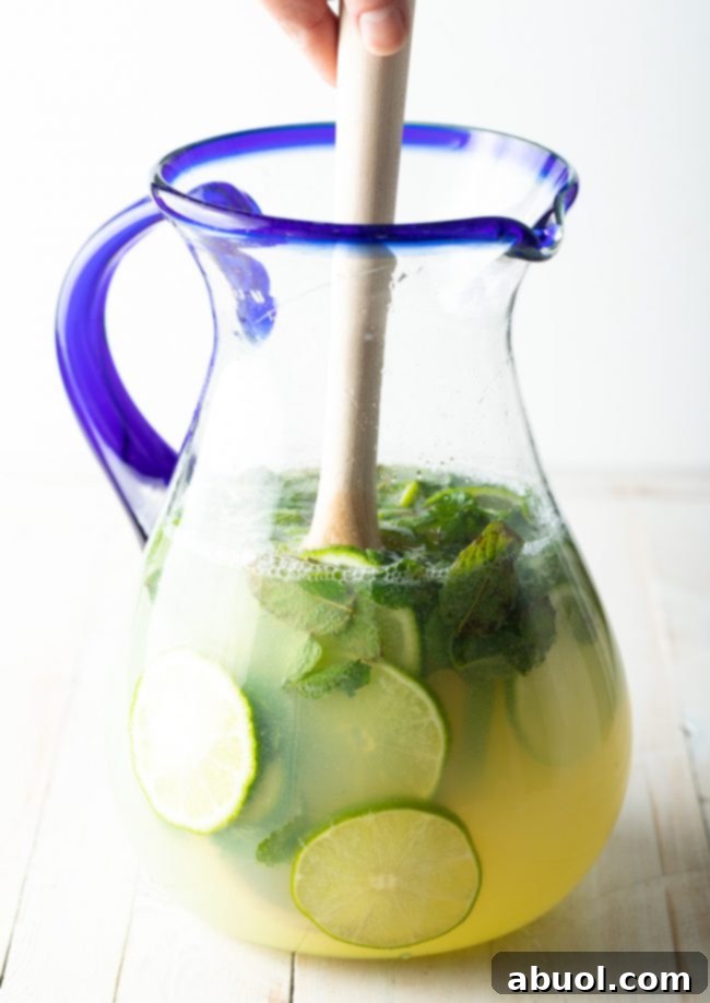 A wooden spoon mixing all of the mojito ingredients together in the pitcher.
