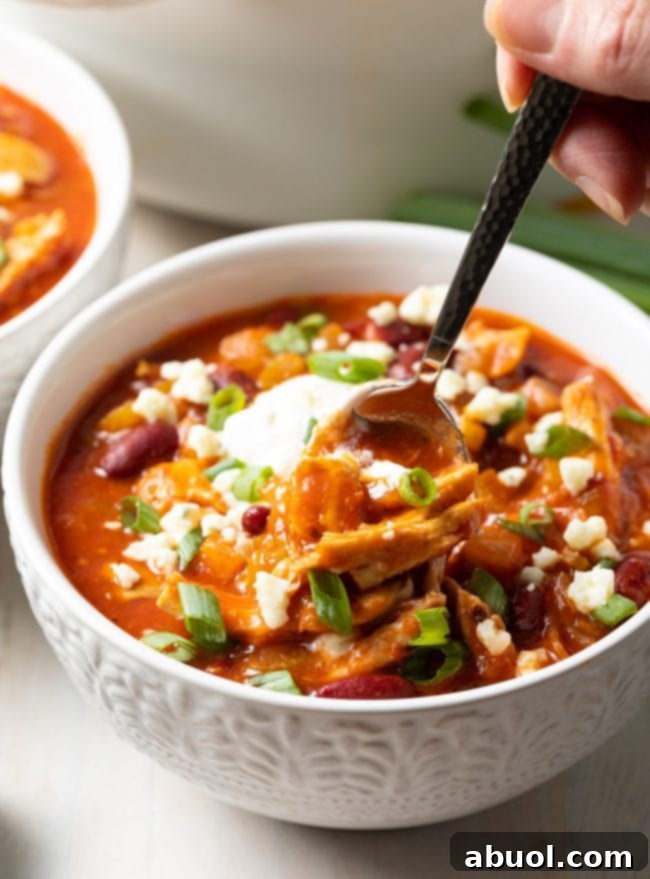 A bowl of rich and creamy chicken chili with buffalo sauce, garnished with fresh herbs.