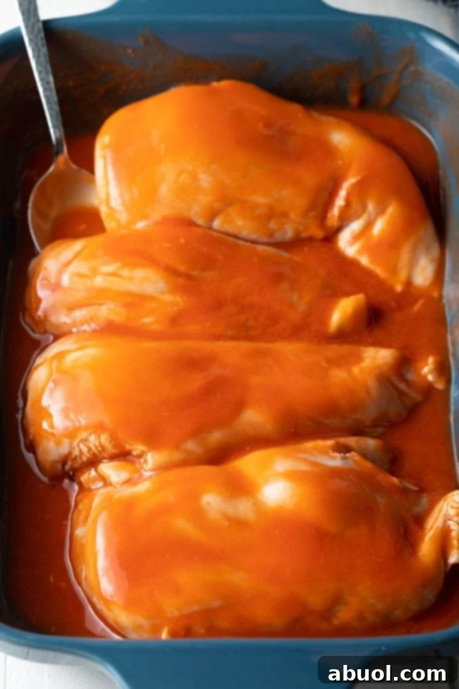 Chicken breasts covered in cayenne pepper sauce, marinating for flavor enhancement.