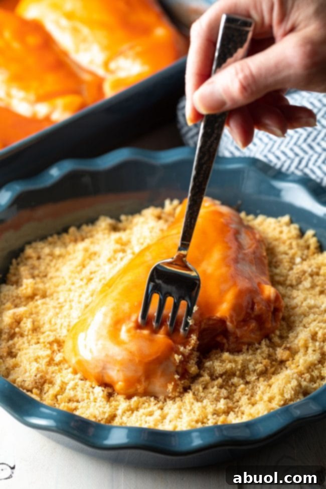 Dipping a chicken breast into Panko crumbs to create a crispy coating.