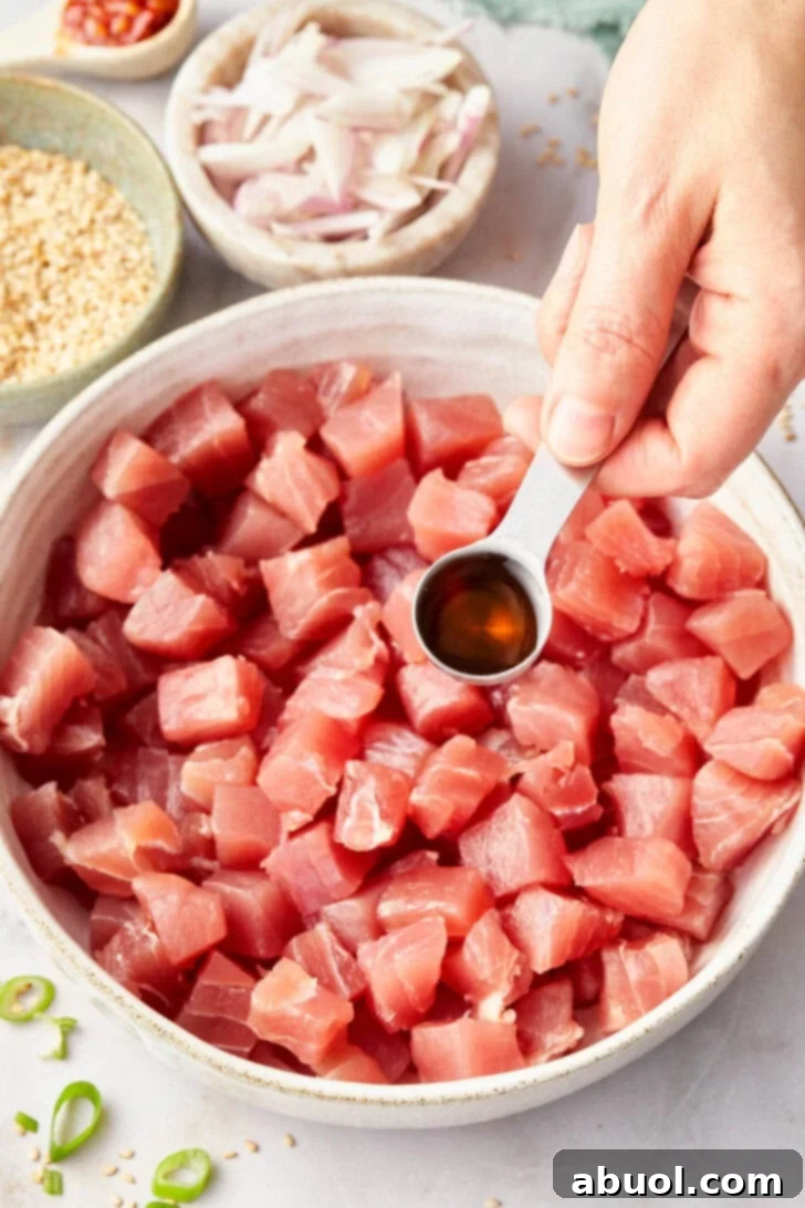 A hand carefully pouring the flavorful sauce over the freshly chopped Ahi tuna, ensuring every piece is evenly coated.