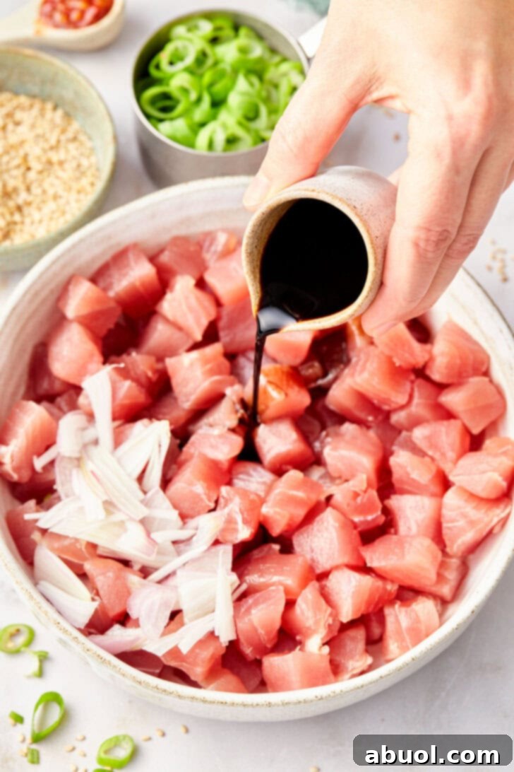 Chopped Ahi tuna mixed with sliced shallots and a generous amount of the savory poke sauce, ready for gentle tossing.