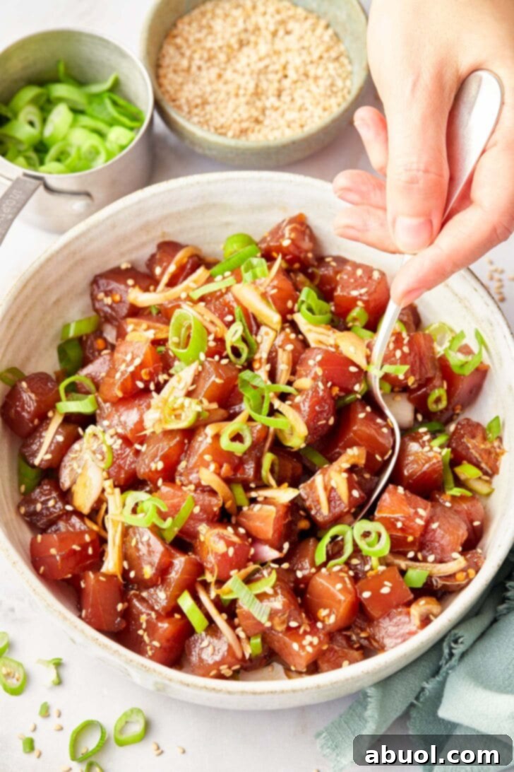 A spoon gently mixing all the ingredients for the poke, ensuring the flavors are well combined without damaging the delicate tuna.