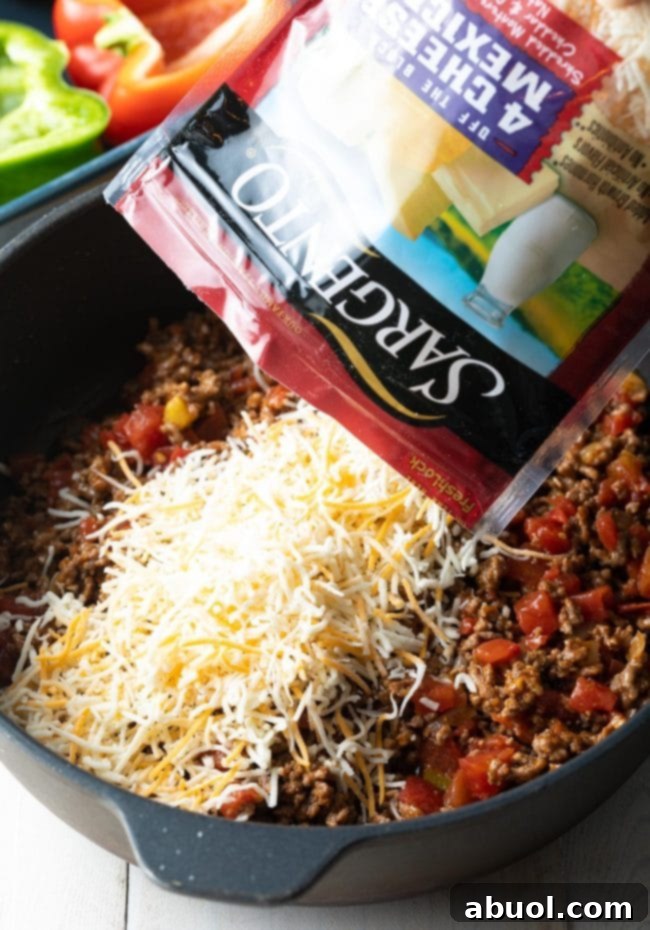 Hearty Keto Stuffed Peppers 6 Close-up of shredded Mexican cheese being mixed into the ground beef and Rotel filling in a skillet.