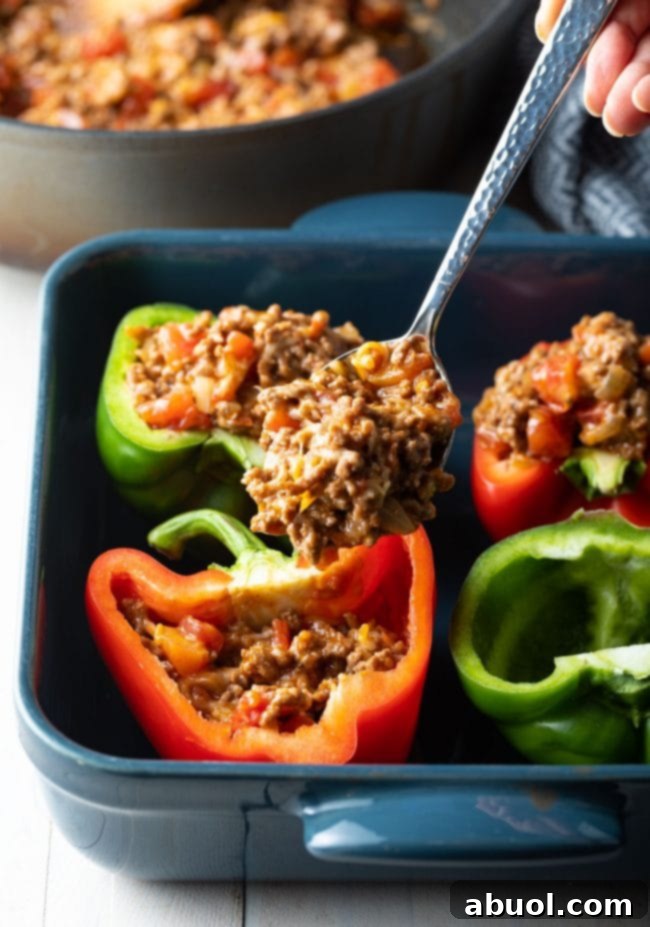 Hearty Keto Stuffed Peppers 7 A spoon scooping the savory meat and cheese filling into a halved bell pepper on a baking dish.