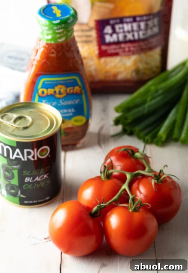 A colorful array of fresh ingredients for Layered Taco Pizza Dip, including ripe on-the-vine tomatoes, a bowl of vibrant salsa, a mound of shredded cheese, a pile of glossy black olives, and crisp whole green onions, showcasing the freshness and quality of the components.