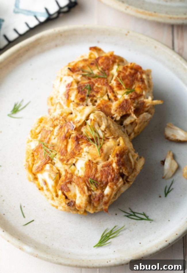 Two crab cakes on a plate topped with fresh dill. 