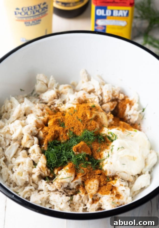 Spices and herbs and mayo added to crab meat in a bowl. 